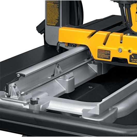 Close-up view of a DEWALT D24000 tile saw showing its rail and cutting platform. The yellow and metallic parts are visible, highlighting the precision mechanics of the tool.