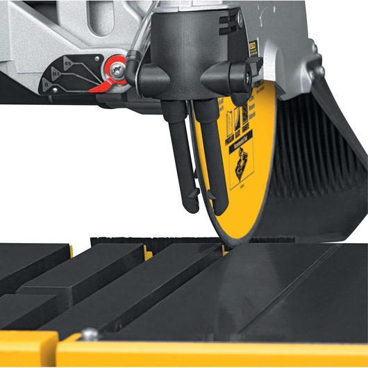 Close-up view of a DEWALT tile saw, focusing on the yellow blade and water nozzles above the cutting surface.