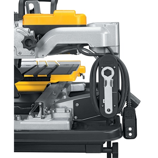 Close-up side view of a DEWALT D24000 tile saw, highlighting its yellow and black components, electric cord, and attached wrench against a white background.
