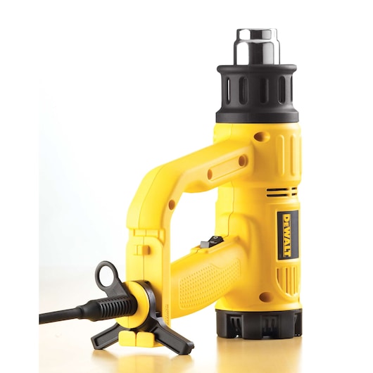 A yellow DEWALT heat gun with a black handle and nozzle, standing upright on a light surface. The tool is electrically powered and features the DEWALT branding on the side.