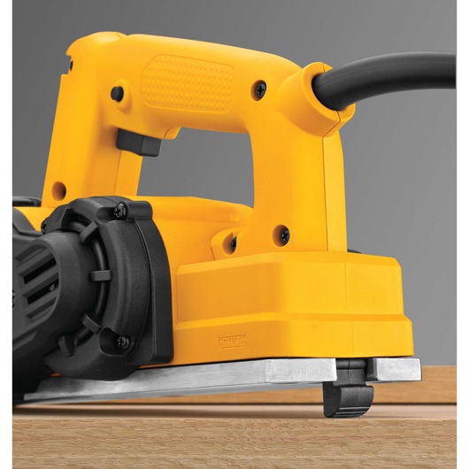 Close-up image of a DEWALT electric hand planer resting on a wooden surface, showing its yellow body, handle, and cord connection.