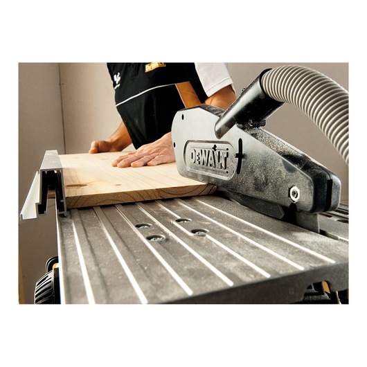 Close-up view of a DEWALT table saw in use, with a person guiding a piece of wood through the saw in a workshop environment.