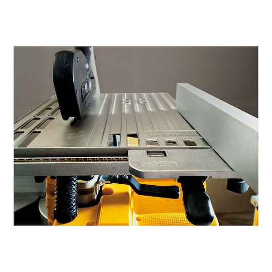 Close-up view of a DEWALT table saw, showing the fence, measurement guide, and part of the cutting surface in a workshop setting.