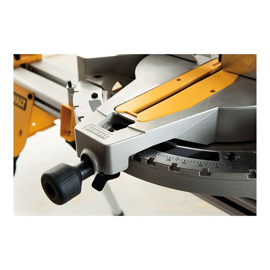 Close-up view of a DEWALT miter saw, showing the angle adjustment handle, scale, and part of the metal and yellow base.