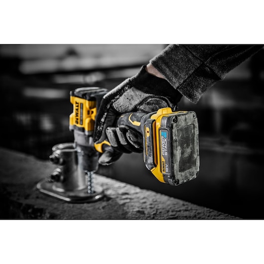 A close-up of a gloved hand using a DEWALT cordless power tool with a POWERSTACK 18V battery to drill a screw into a metal