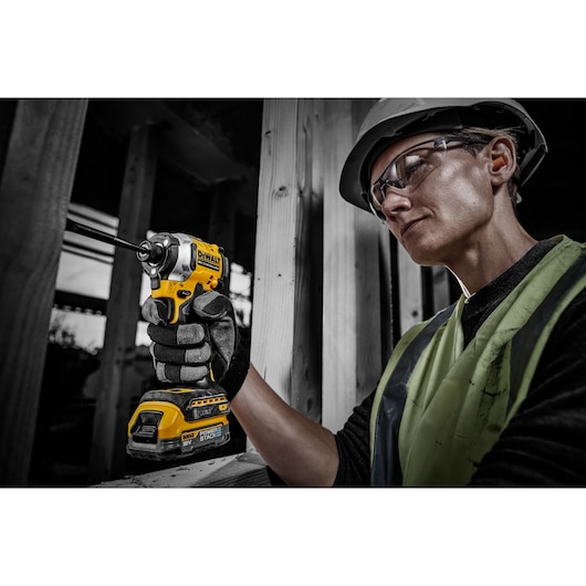 Person wearing a safety helmet and vest using a DEWALT Powerstack cordless impact driver drill inside a construction site
