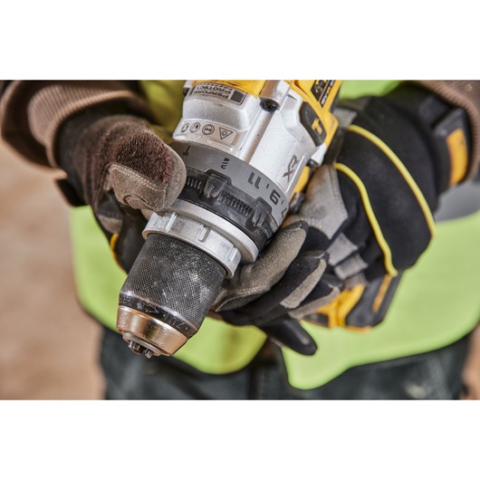 Close-up view of a person wearing work gloves holding a DEWALT cordless drill, focusing on the adjustable torque collar and drill chuck.