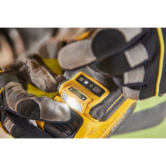 Close-up of a person wearing work gloves operating a DEWALT power tool, showing the illuminated control panel and function buttons.