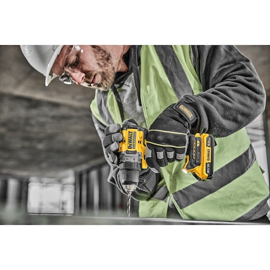 A person wearing a safety vest and gloves is using a DEWALT cordless drill (model DCD800D2T) at a construction site.