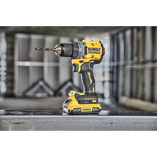 A DEWALT cordless power drill with a drill bit attached, standing upright on a metal surface in an industrial or construction setting.