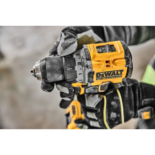 Close-up view of a person wearing work gloves holding a DEWALT 18V XR brushless cordless drill, model DCD800D2T, during use.