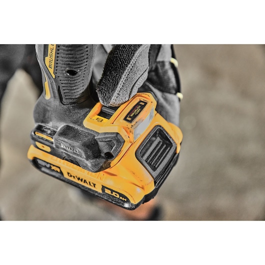 Close-up of a gloved hand holding a DEWALT cordless power drill featuring a brushless motor and a 2.0 Ah battery pack.