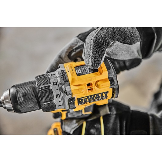 Close-up view of a DEWALT cordless power drill being adjusted by a person wearing work gloves.