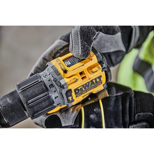 A close-up of a worker's gloved hand adjusting the speed setting on a DEWALT 18V XR brushless power drill.