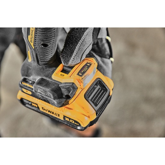 Close-up of a gloved hand holding a DEWALT cordless power tool with a visible 20V 2.0Ah lithium-ion battery attached.