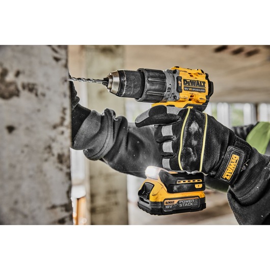 A person wearing protective gloves is using a DEWALT cordless power drill to drill into a metal surface in a construction setting.