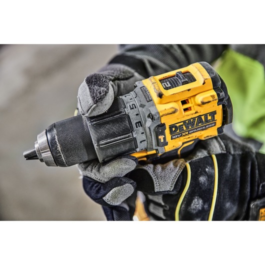 Close-up of a person wearing work gloves holding a yellow and black DEWALT 18V XR brushless cordless drill.