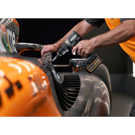 Close-up of a person using a DEWALT cordless drill on a part of an orange and black vehicle, possibly a race car.
