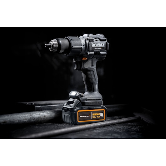 A DEWALT cordless power drill with 18V XR battery, featuring McLaren branding, standing upright on a dark industrial surface.