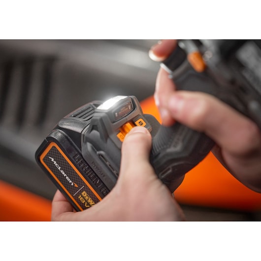 Close-up image of a person adjusting the controls on a DEWALT 18V cordless tool with an integrated LED work light. The tool features McLaren branding and orange detail accents.