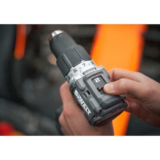 A close-up view of a person's hand adjusting the speed setting on a DEWALT cordless power drill. The drill is labeled with numbers and has a visible battery pack.