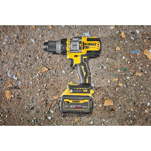 A DEWALT cordless power drill with a FlexVolt XR Lithium-Ion 18V/54V battery is placed on a rough, debris-covered surface.