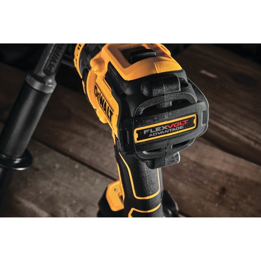 Close-up of a DEWALT cordless power drill, showing the handle and FLEXVOLT Advantage label. The tool is mostly yellow and black, placed on a wooden surface.
