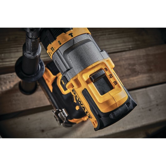 Close-up of a DEWALT cordless power drill showing its grip, speed settings, and part of the side handle, positioned against a wooden background.