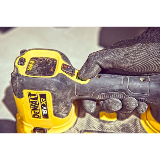 Close-up view of a gloved hand holding and pressing a button on a DEWALT 18V XR cordless power tool, with yellow and black color design.