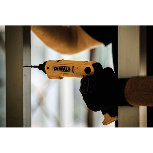 A person using a DEWALT yellow cordless screwdriver to drill into a metal frame, wearing protective gloves.