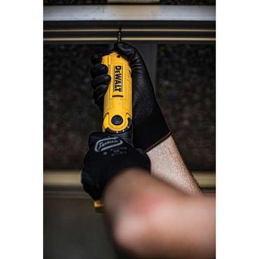 A person wearing black work gloves uses a yellow DEWALT cordless screwdriver to drive a screw into a metal frame.