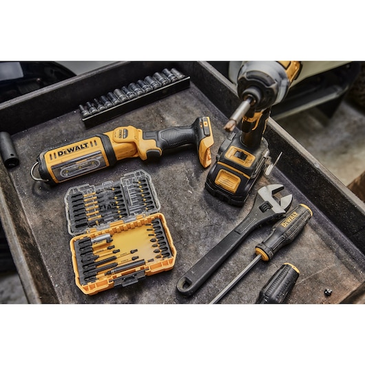A DEWALT cordless impact driver, a DEWALT tool kit with various bits, a DEWALT adjustable wrench, and a DEWALT screwdriver are arranged on a metal tray. Additional sockets and tools are visible in the background. The setting appears to be a workshop.
