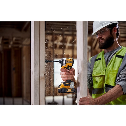 Person uses DEWALT cordless drill to bore a hole in a wooden beam at a construction site.