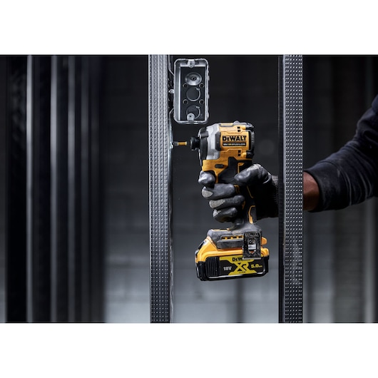 Gloved hand using a DEWALT cordless impact driver on a metal frame near an electrical box.