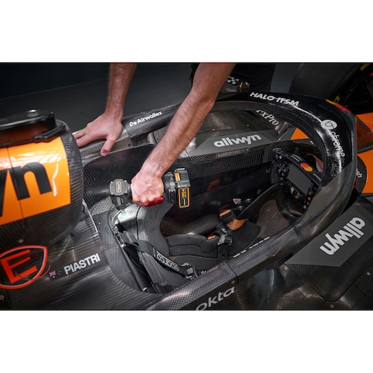 A person uses a DEWALT cordless tool to work inside the cockpit of a racing car. The focus is on the tool and the car's
