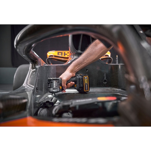A person using a DEWALT cordless power tool inside the cockpit of a race car, focusing on the interior and carbon fibre