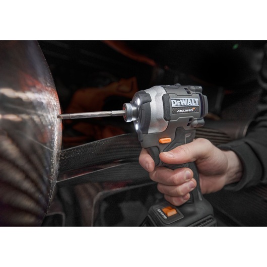 Hand using a DEWALT McLaren cordless impact driver on a metallic surface.