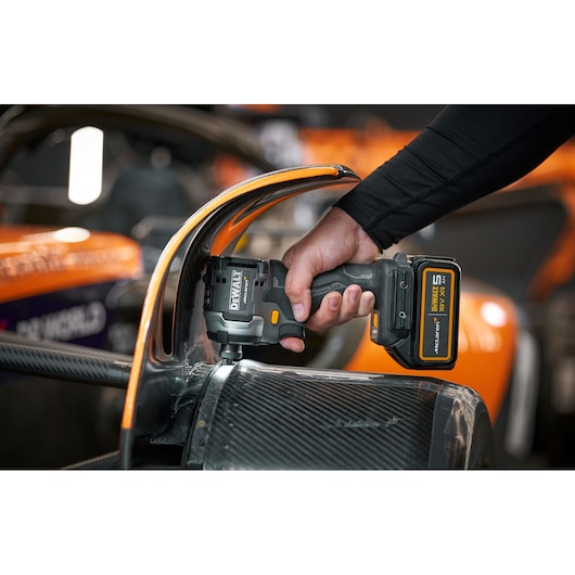 A person is using a DEWALT cordless power tool with an XR lithium-ion battery to work on a carbon fiber component of an