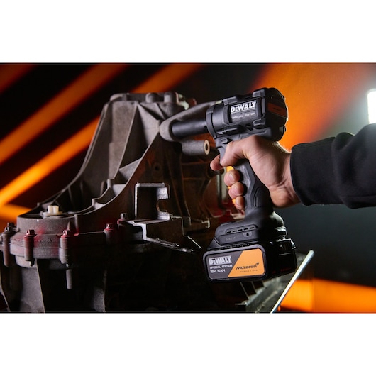 DEWALT tool held by hand near machinery, SKUs DCF92MP2T-QW, DCF92MP2T, photography category, orange background.