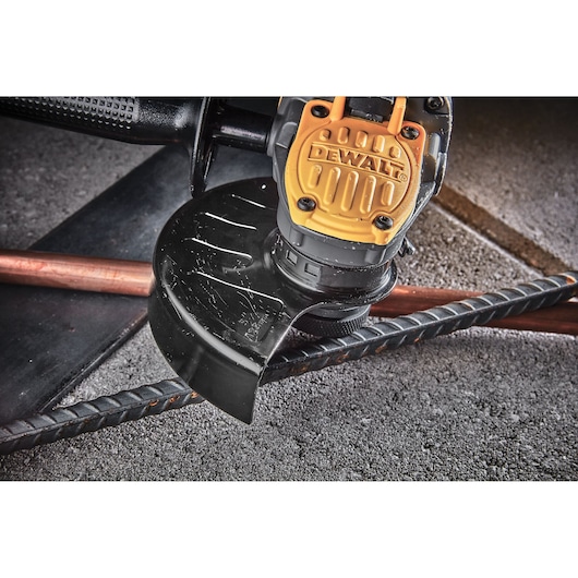 DEWALT angle grinder cutting rebar and copper pipe on a rough concrete surface.
