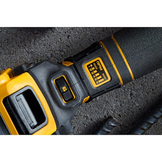 Close-up image of a DEWALT power tool showing its speed setting dial and RPM indicator, with a concrete surface and metal rods in the background.