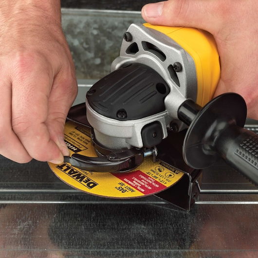 Close-up of hands adjusting a DEWALT angle grinder with a yellow and black abrasive disc.