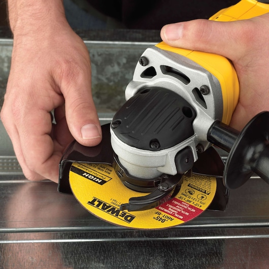 Close-up of hands holding a DEWALT angle grinder with a yellow cutting disc, preparing to cut a metal surface.