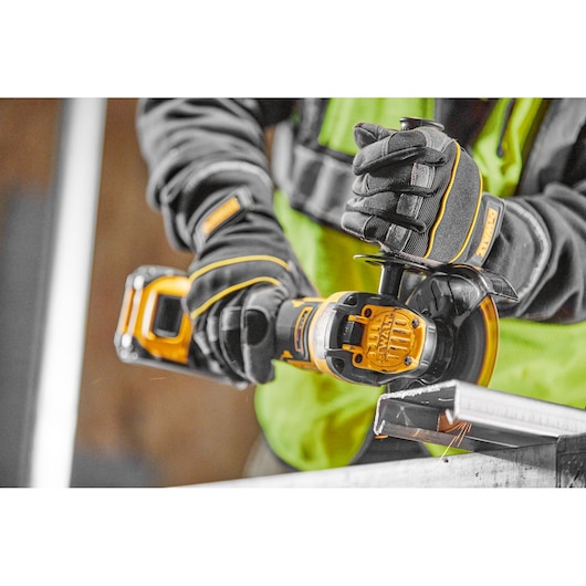 A close-up view of a person wearing protective gloves and a high-visibility vest using a DEWALT cordless angle grinder to