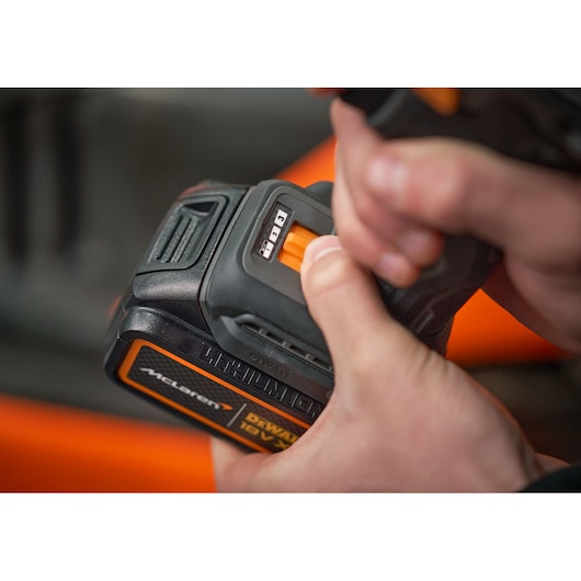Close-up of hands holding a DEWALT 18V XR Lithium-Ion power tool battery from the McLaren series, adjusting a control switch on the battery.