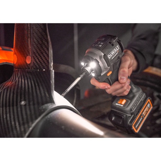 A close-up of a person using a DEWALT cordless power drill with LED lights to work on a carbon fiber structure, possibly part of a vehicle or machinery.