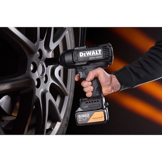 A DEWALT power tool is used to tighten a car wheel nut. Hand holding tool beside alloy wheel.