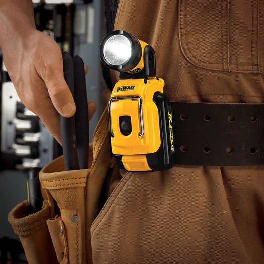 A DEWALT DCL510N compact yellow LED work light clipped onto a tool belt worn by a person dressed in brown workwear. The
