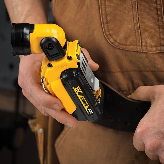 A person attaches a DEWALT DCL510N 12V cordless LED work light to their belt. The compact yellow and black device is