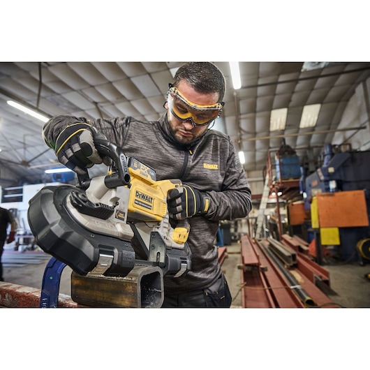 DEWALT DCS374N, DCS374N-XJ band saw in use cutting metal pipe in workshop, industrial background visible.
